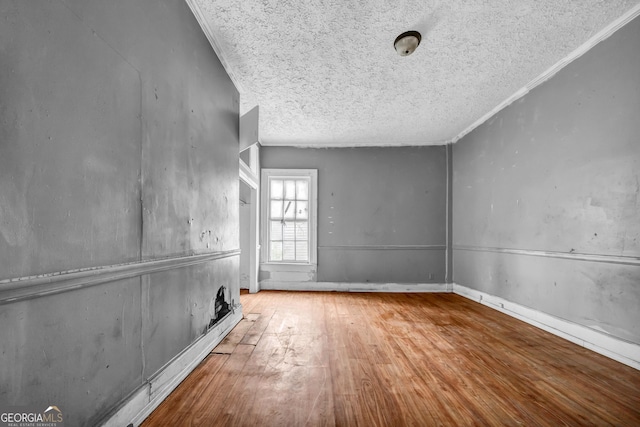 empty room featuring a textured ceiling, light hardwood / wood-style flooring, and ornamental molding