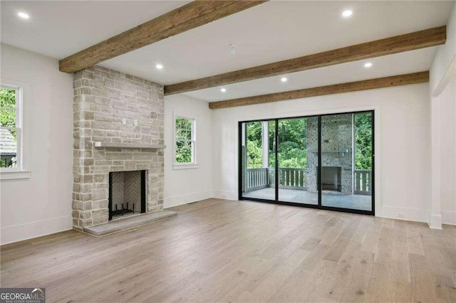 unfurnished living room with light hardwood / wood-style floors, a stone fireplace, and beam ceiling