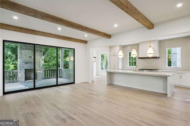 kitchen featuring white cabinets, light wood-type flooring, hanging light fixtures, and a healthy amount of sunlight