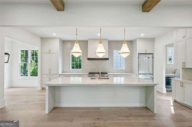 kitchen with beam ceiling, a kitchen island with sink, and sink