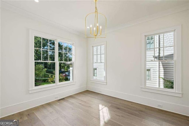 unfurnished dining area with a healthy amount of sunlight, hardwood / wood-style floors, a chandelier, and ornamental molding