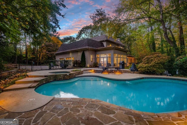 pool at dusk with an in ground hot tub and a patio