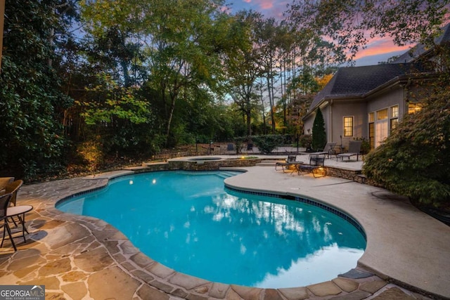 pool at dusk with a patio area and an in ground hot tub