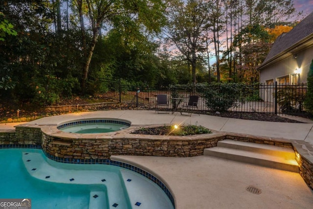 pool at dusk featuring a patio area and an in ground hot tub