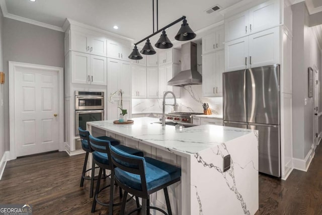 kitchen featuring white cabinets, an island with sink, wall chimney exhaust hood, and stainless steel appliances