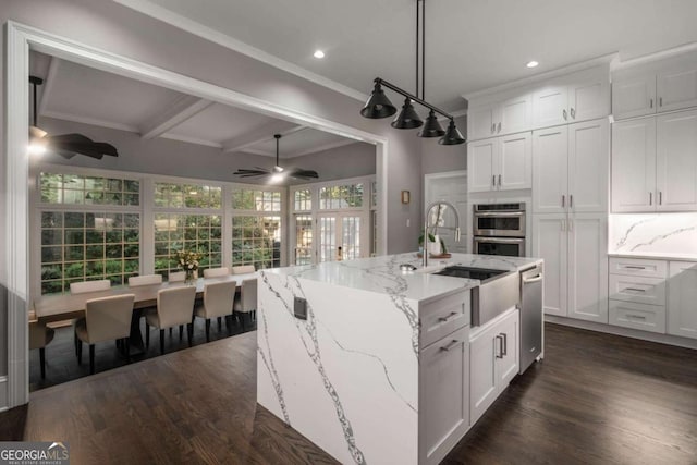 kitchen with beam ceiling, white cabinetry, sink, and an island with sink