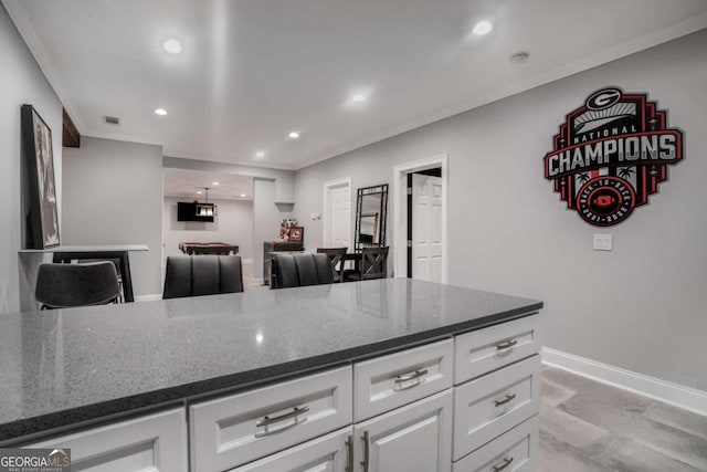 kitchen featuring white cabinetry, ornamental molding, and dark stone counters