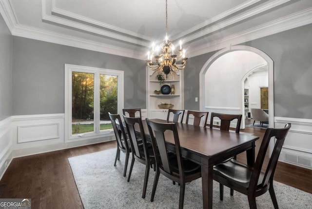 dining area featuring dark hardwood / wood-style flooring, ornamental molding, a tray ceiling, an inviting chandelier, and built in features