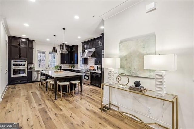 kitchen featuring a kitchen bar, appliances with stainless steel finishes, light wood-type flooring, a kitchen island, and range hood