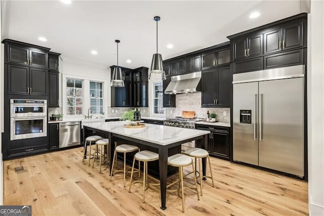 kitchen featuring appliances with stainless steel finishes, a breakfast bar, extractor fan, decorative light fixtures, and a center island