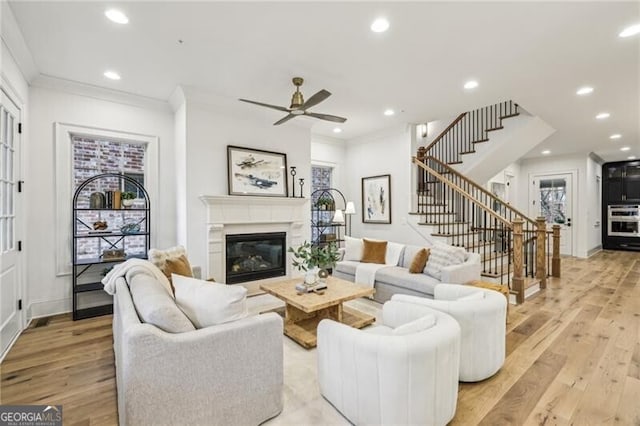 living room featuring a tile fireplace, light wood-type flooring, ceiling fan, and crown molding