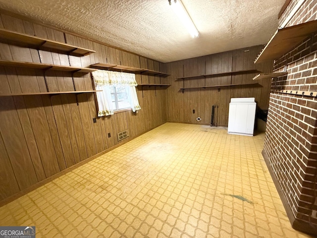 basement with a textured ceiling, wood walls, and fridge