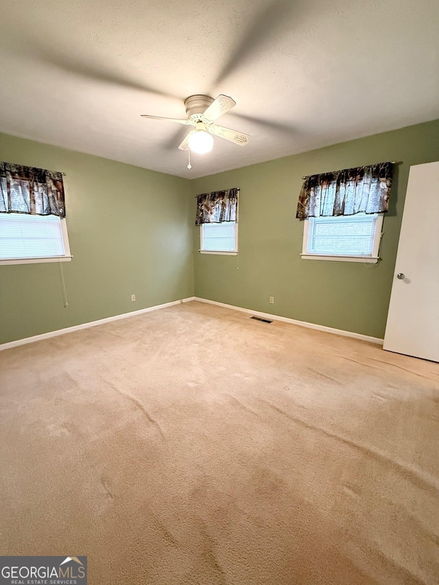 carpeted empty room with ceiling fan and plenty of natural light