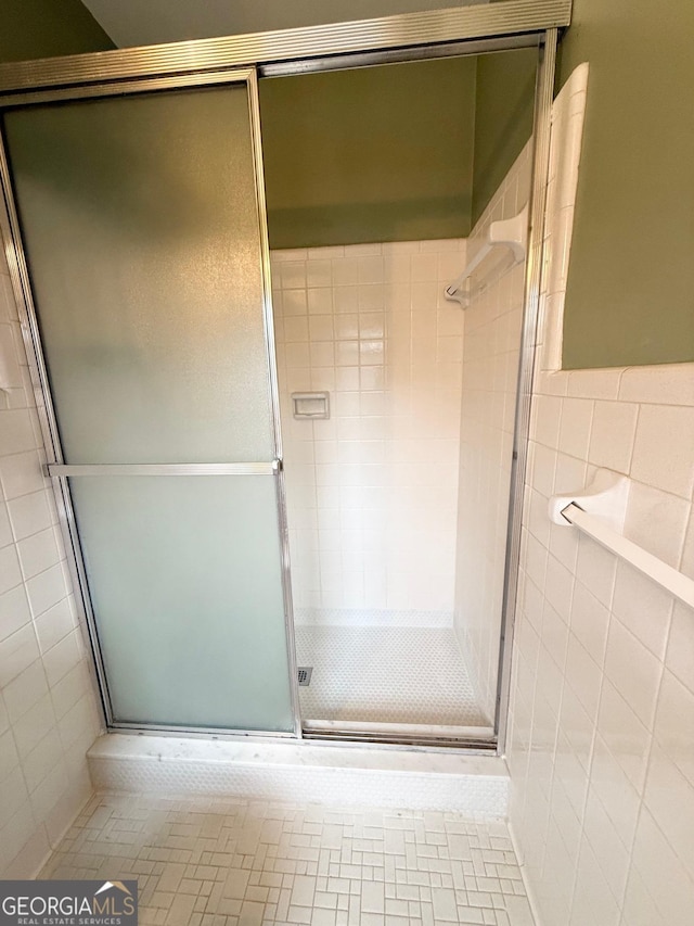 bathroom featuring tile patterned floors, a shower with door, and tile walls