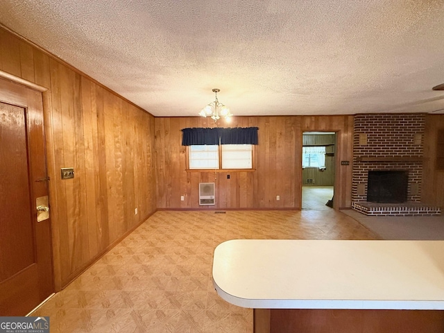 unfurnished living room featuring heating unit, wooden walls, a notable chandelier, and a brick fireplace