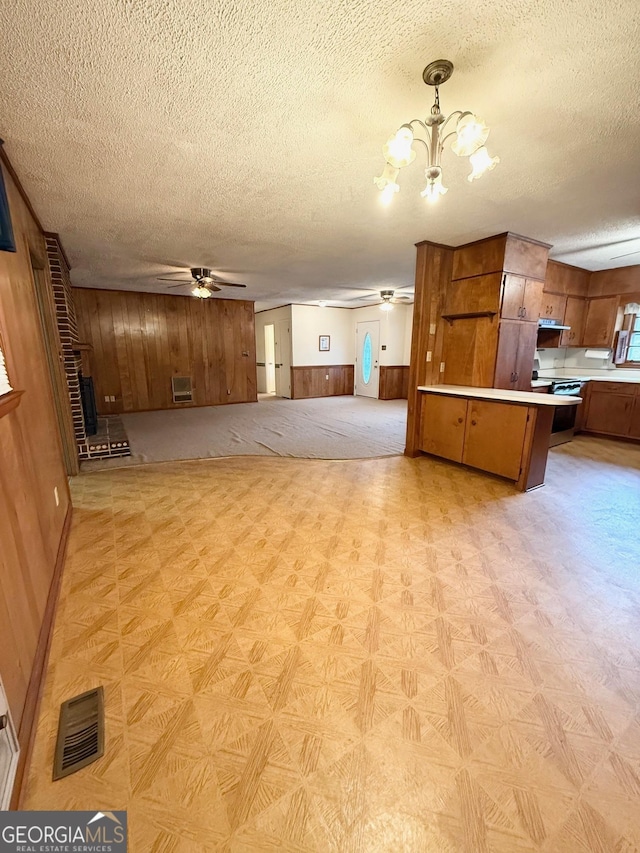 unfurnished living room with a textured ceiling, wooden walls, a wall unit AC, and ceiling fan with notable chandelier