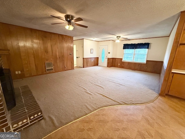 empty room featuring ceiling fan, wooden walls, a textured ceiling, and a brick fireplace