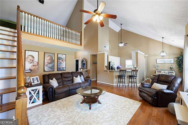 living room with a textured ceiling, high vaulted ceiling, wood-type flooring, and ceiling fan with notable chandelier