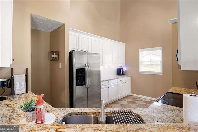 kitchen featuring light stone counters, sink, white cabinetry, and stainless steel refrigerator with ice dispenser