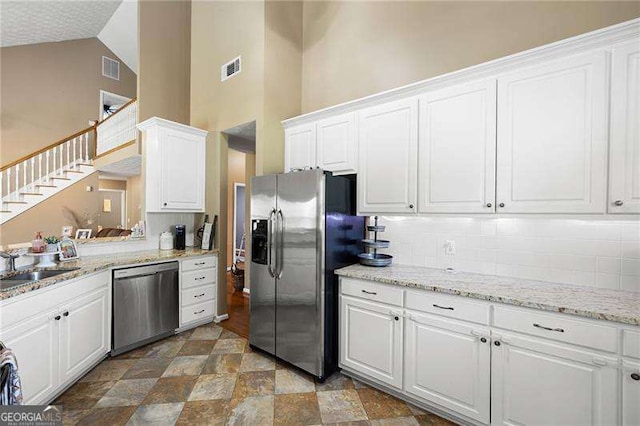 kitchen with sink, tasteful backsplash, high vaulted ceiling, white cabinets, and appliances with stainless steel finishes