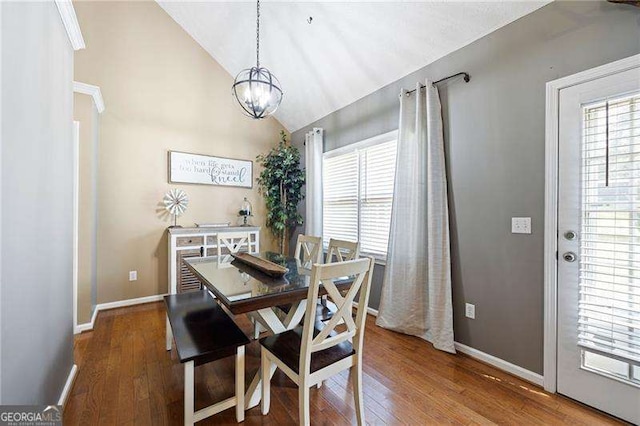 dining room with hardwood / wood-style floors, vaulted ceiling, and an inviting chandelier