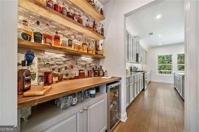 bar with gray cabinets, dark hardwood / wood-style floors, butcher block counters, beverage cooler, and stainless steel range oven