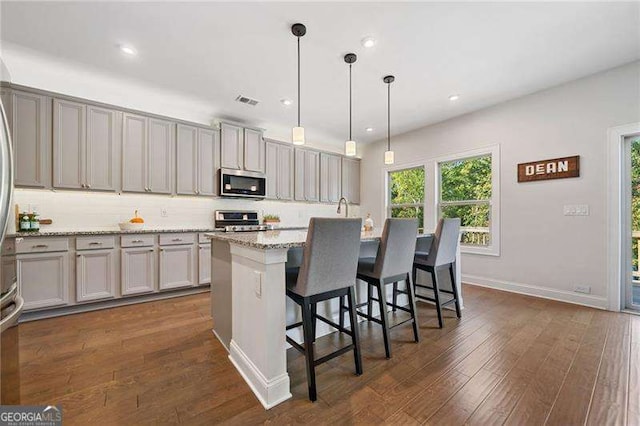 kitchen featuring a breakfast bar area, appliances with stainless steel finishes, a kitchen island with sink, light stone counters, and decorative light fixtures