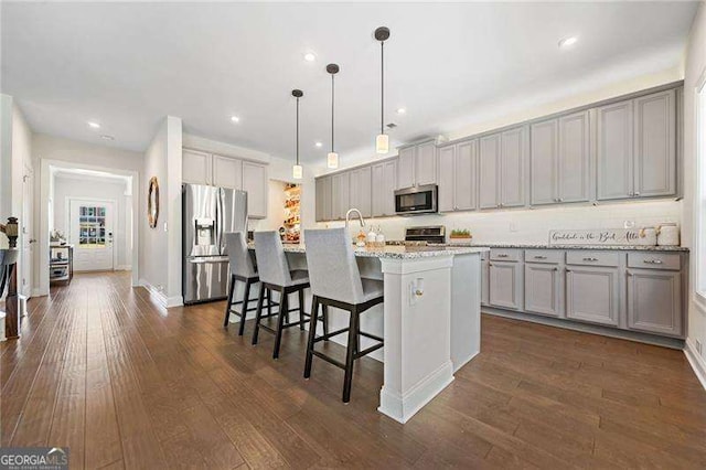 kitchen with a breakfast bar, gray cabinetry, hanging light fixtures, a kitchen island with sink, and stainless steel appliances