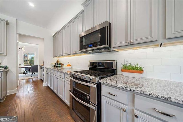 kitchen featuring gray cabinetry, backsplash, dark hardwood / wood-style flooring, stainless steel appliances, and light stone countertops