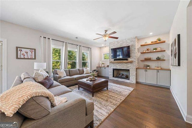 living room featuring a stone fireplace, dark hardwood / wood-style floors, and ceiling fan