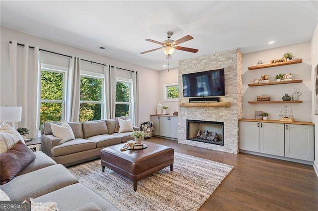 living room featuring dark wood-type flooring, a large fireplace, and ceiling fan