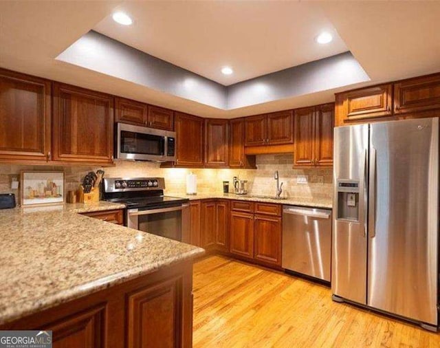 kitchen with appliances with stainless steel finishes, tasteful backsplash, sink, light stone counters, and light hardwood / wood-style flooring