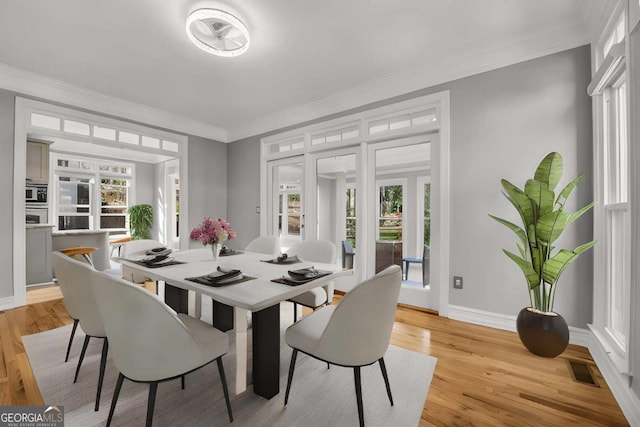 dining area featuring a wealth of natural light, ornamental molding, and light wood-type flooring