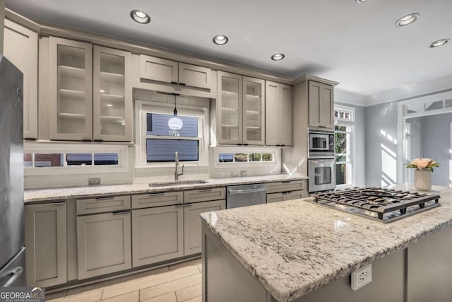 kitchen with stainless steel appliances, light stone counters, ornamental molding, and sink