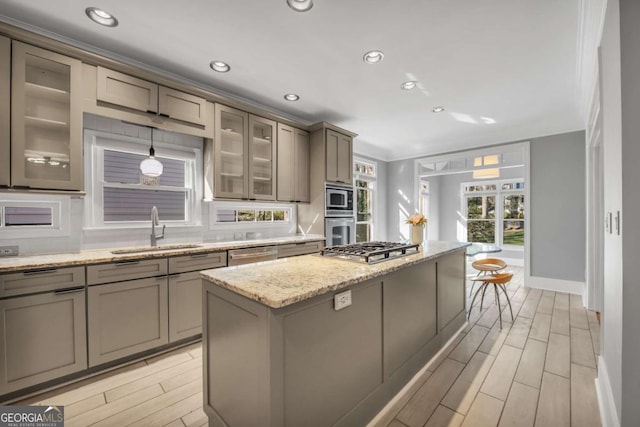 kitchen featuring sink, ornamental molding, appliances with stainless steel finishes, a kitchen island, and light stone counters