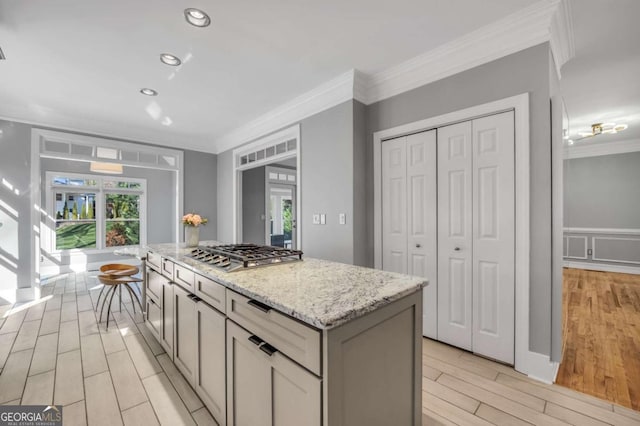 kitchen with stainless steel gas stovetop, a center island, light stone counters, and ornamental molding