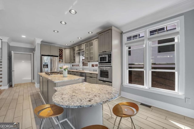 kitchen featuring light stone countertops, a center island, crown molding, a breakfast bar, and appliances with stainless steel finishes