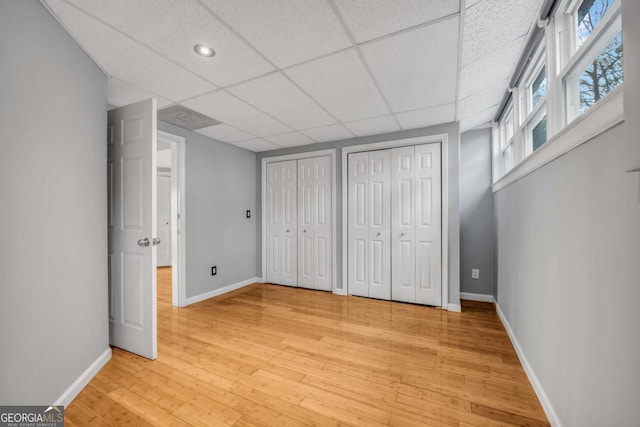 unfurnished bedroom with hardwood / wood-style floors, a drop ceiling, and multiple closets