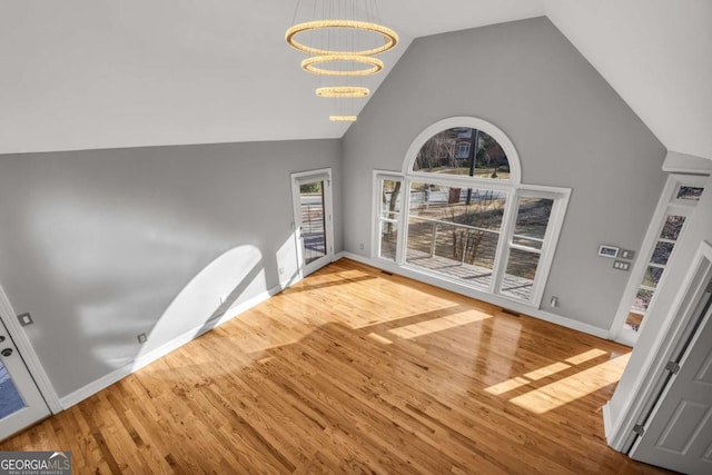 unfurnished living room with a chandelier, wood-type flooring, and lofted ceiling