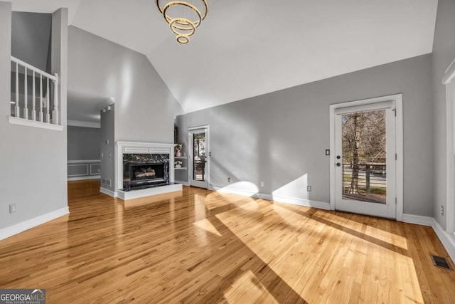 unfurnished living room with wood-type flooring, a fireplace, high vaulted ceiling, and a chandelier