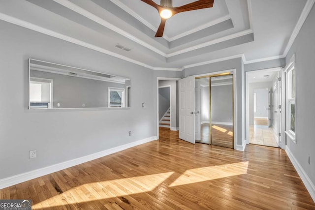 unfurnished bedroom featuring ceiling fan, a raised ceiling, light hardwood / wood-style floors, a closet, and ornamental molding