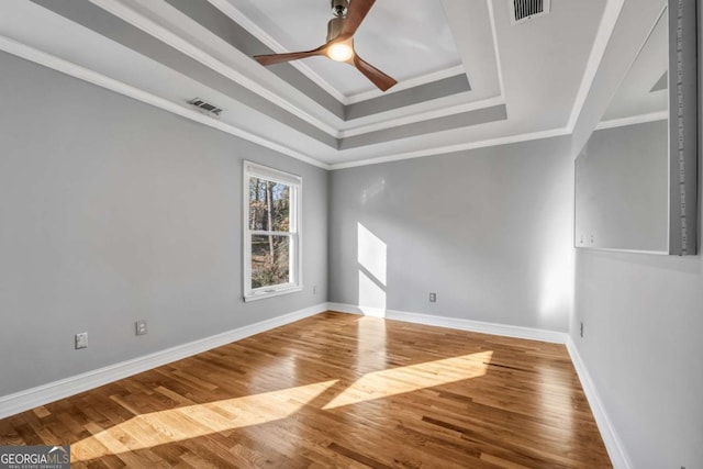 spare room featuring hardwood / wood-style floors, ceiling fan, crown molding, and a tray ceiling