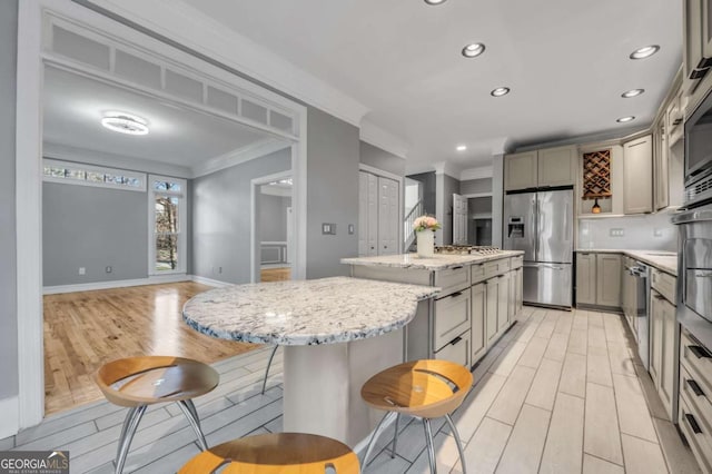 kitchen featuring light stone countertops, appliances with stainless steel finishes, gray cabinets, a kitchen island, and ornamental molding