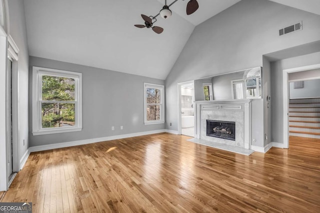 unfurnished living room featuring a fireplace, light hardwood / wood-style flooring, high vaulted ceiling, and ceiling fan