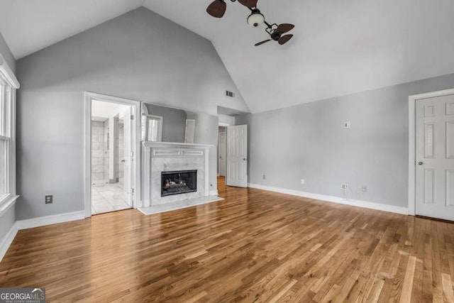 unfurnished living room featuring ceiling fan, a premium fireplace, high vaulted ceiling, and light hardwood / wood-style flooring