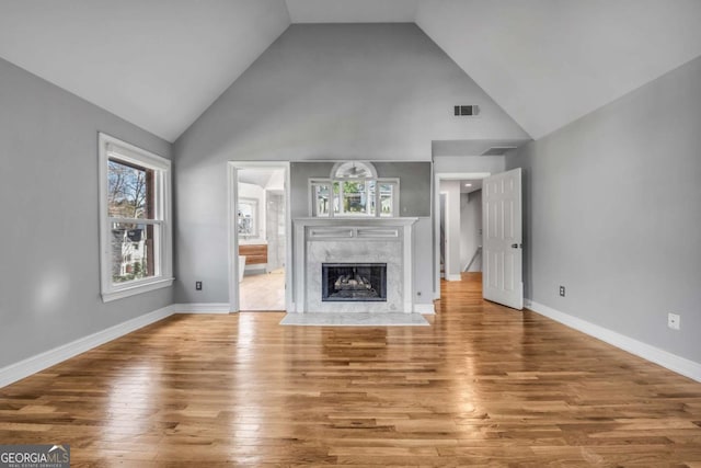 unfurnished living room with wood-type flooring, high vaulted ceiling, and a premium fireplace