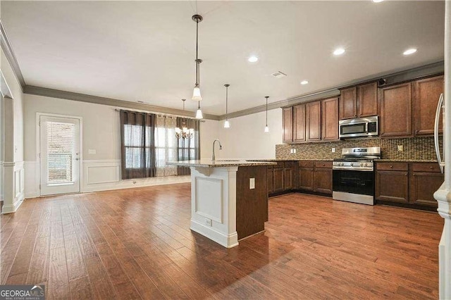 kitchen featuring appliances with stainless steel finishes, ornamental molding, decorative light fixtures, stone counters, and a breakfast bar area