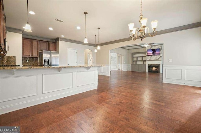 kitchen with stainless steel fridge, light stone counters, crown molding, a chandelier, and hanging light fixtures