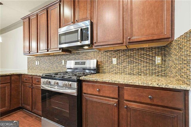 kitchen featuring light stone countertops, dark wood-type flooring, stainless steel appliances, crown molding, and decorative backsplash