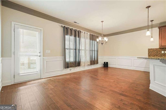 unfurnished dining area featuring dark wood-type flooring, an inviting chandelier, and crown molding